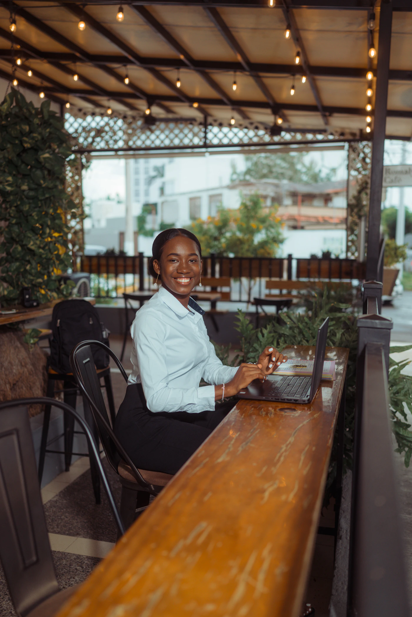 A smiling woman working on her laptop at an outdoor café